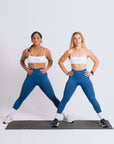 Two women in matching blue workout gear standing on a mat, getting ready to exercise.