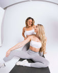 Two women in female activewear hugging in a studio setting.