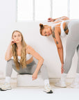 Two women wearing grey leggings and white sports bras, ready to conquer her workout in style.