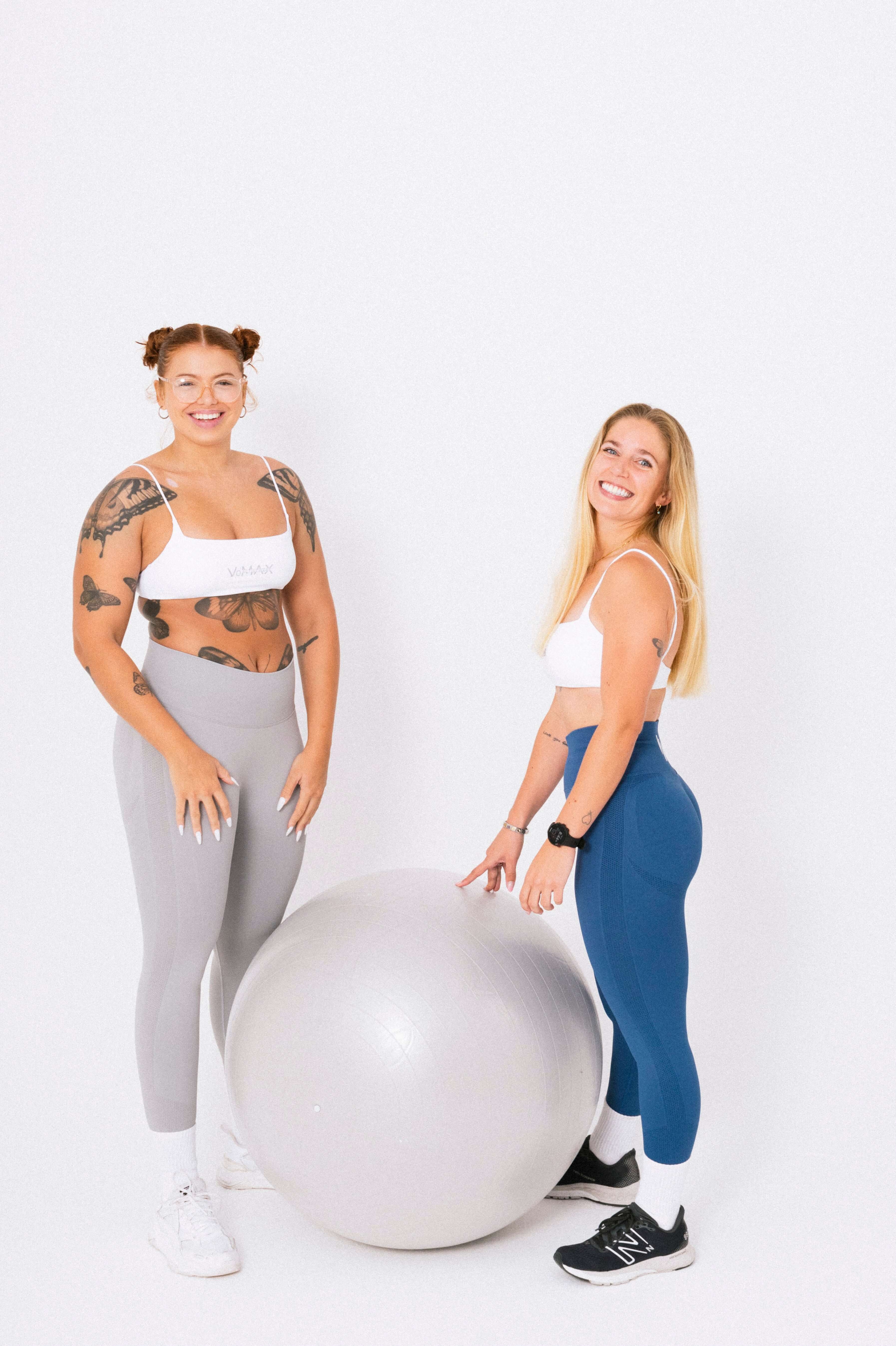 Two women in sports bras and leggings striking a pose on a ball. Female activewear.