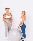 Two women in sports bras and leggings striking a pose on a ball. Female activewear.