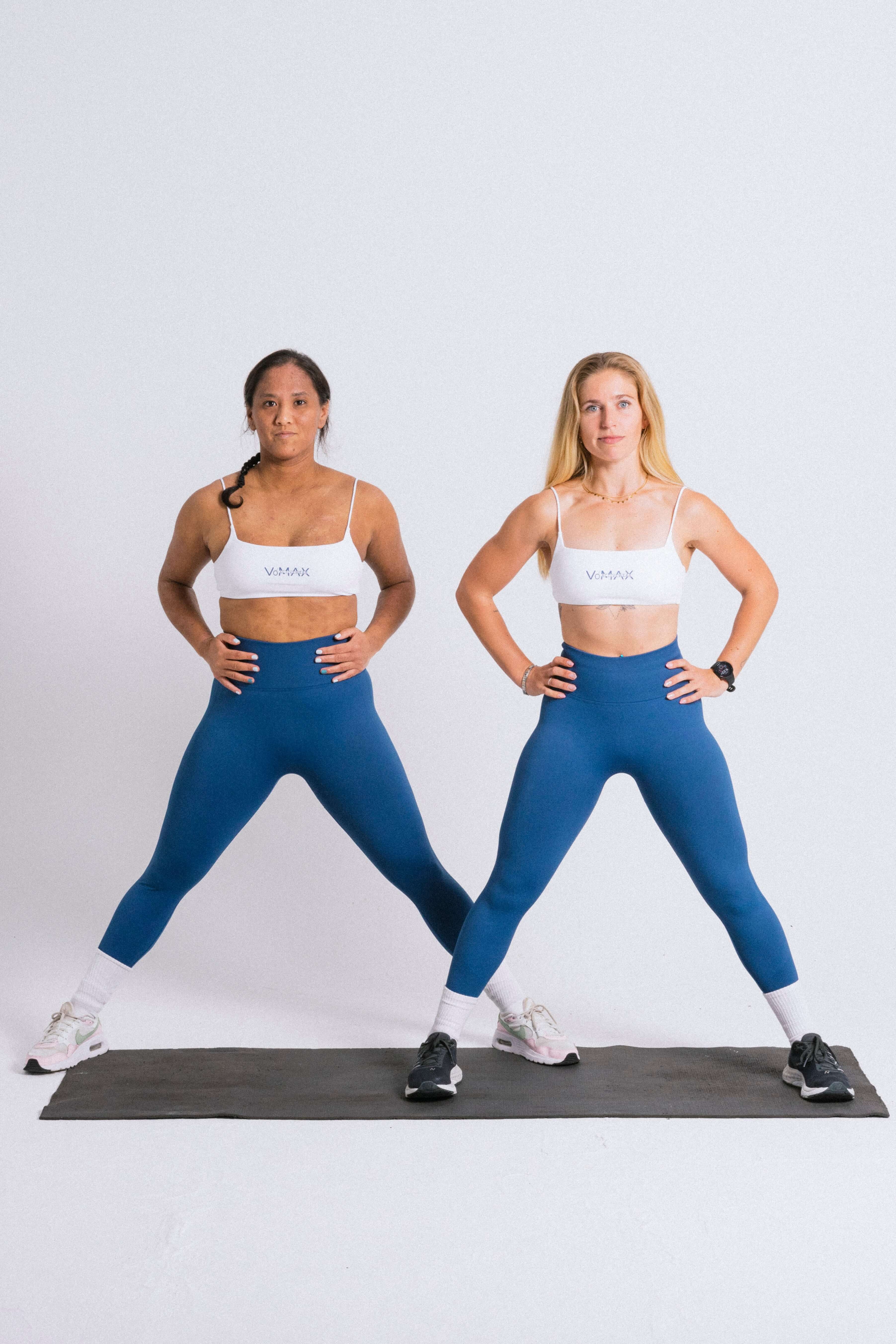  Two women in matching blue workout gear standing on a mat, getting ready to exercise.