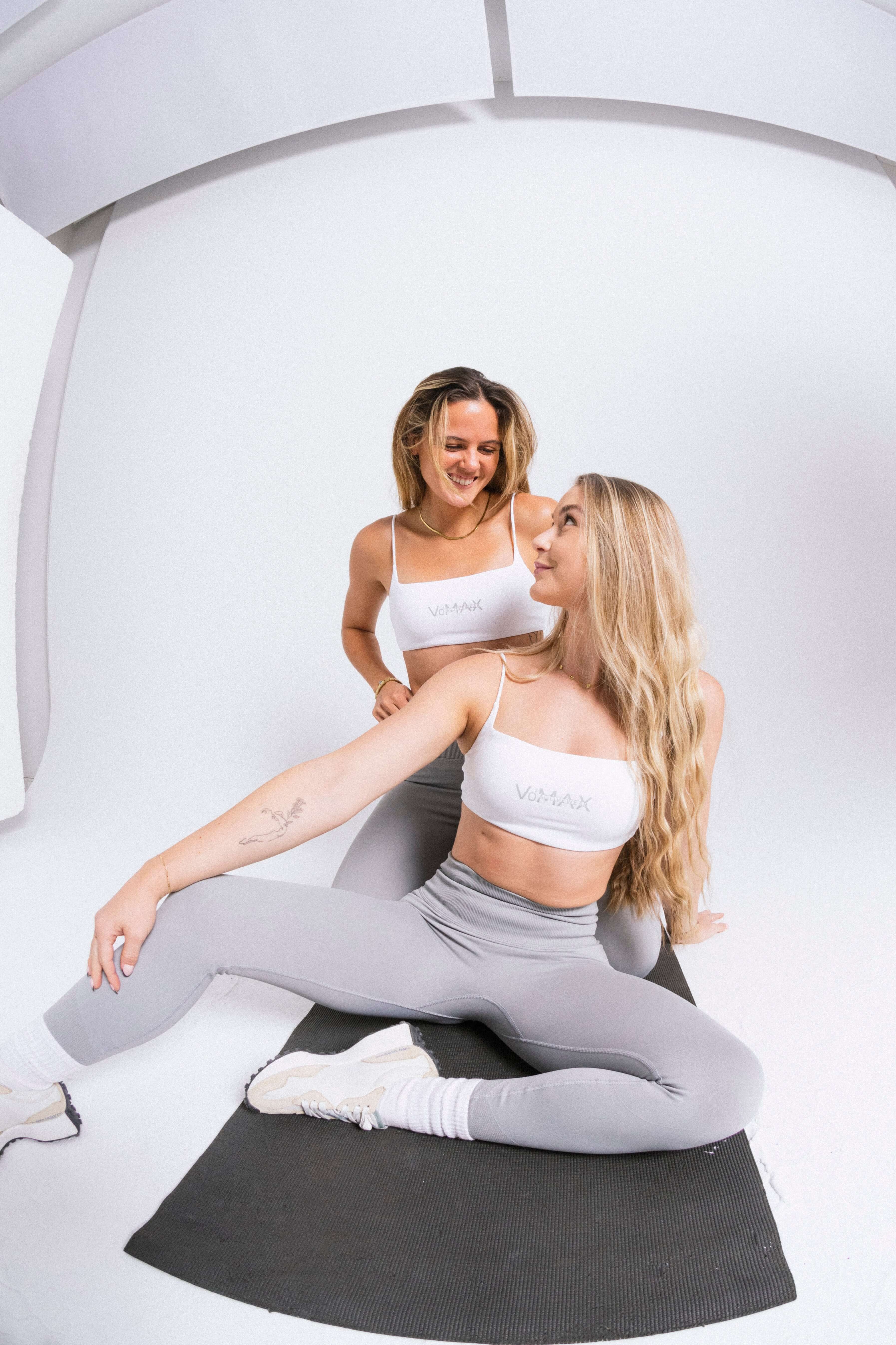 Two women in female activewear hugging in a studio setting.