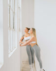 Stylish female activewear: Two women in grey leggings posing by a window.