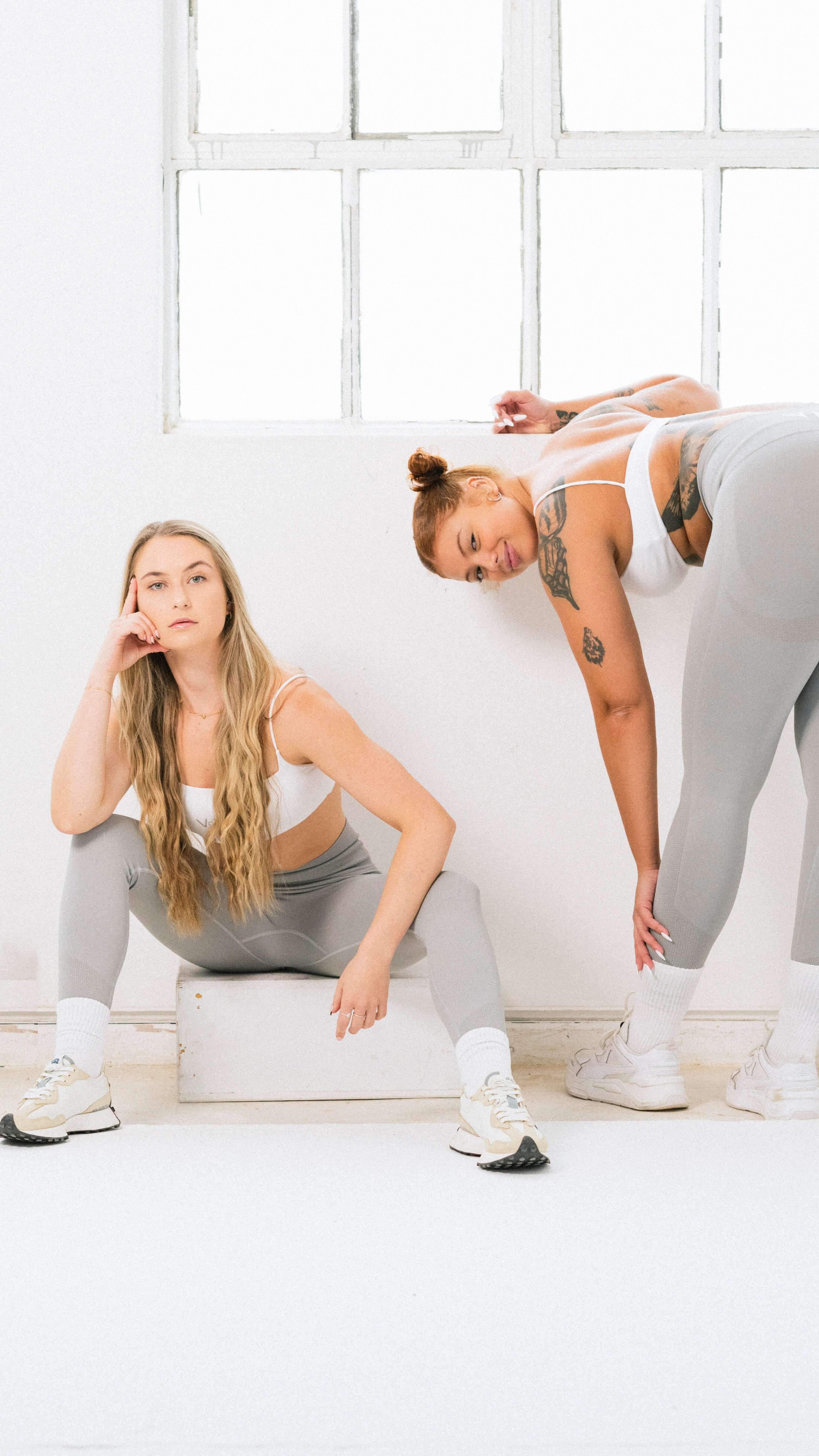 Two women wearing grey leggings and white sports bras, ready to conquer her workout in style.