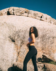 A fit female posing on a rock in black drawstring leggings and a pastel lilac sports bra.