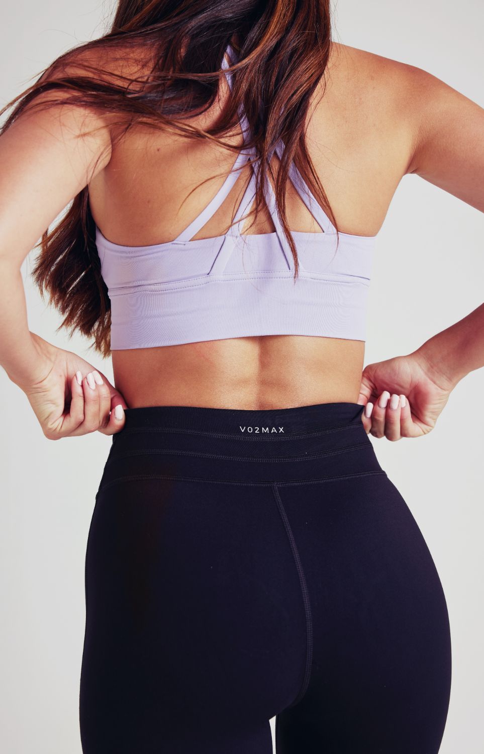 A fit woman in black drawstring leggings and a pastel lilac sports bra.