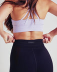 A fit woman in black drawstring leggings and a pastel lilac sports bra.